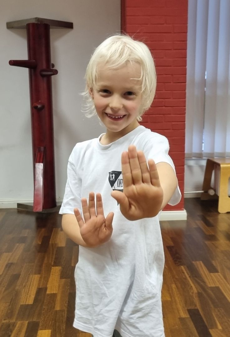 Ein blondes Kind steht in Kampfstellung mit offenen Händen vor einer Trainingswand.